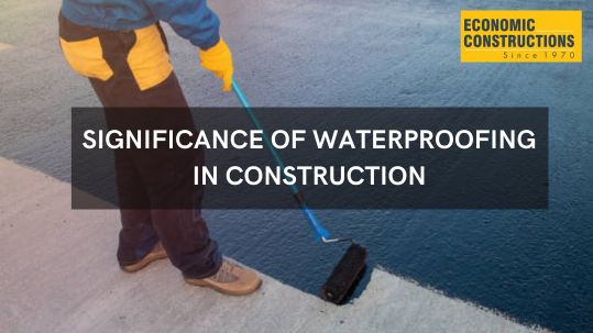 Construction worker applying waterproofing material to a foundation wall, highlighting the importance of preventing water damage. Economic Constructions emphasizes the cost-saving benefits and long-term durability achieved through proper waterproofing techniques in building projects